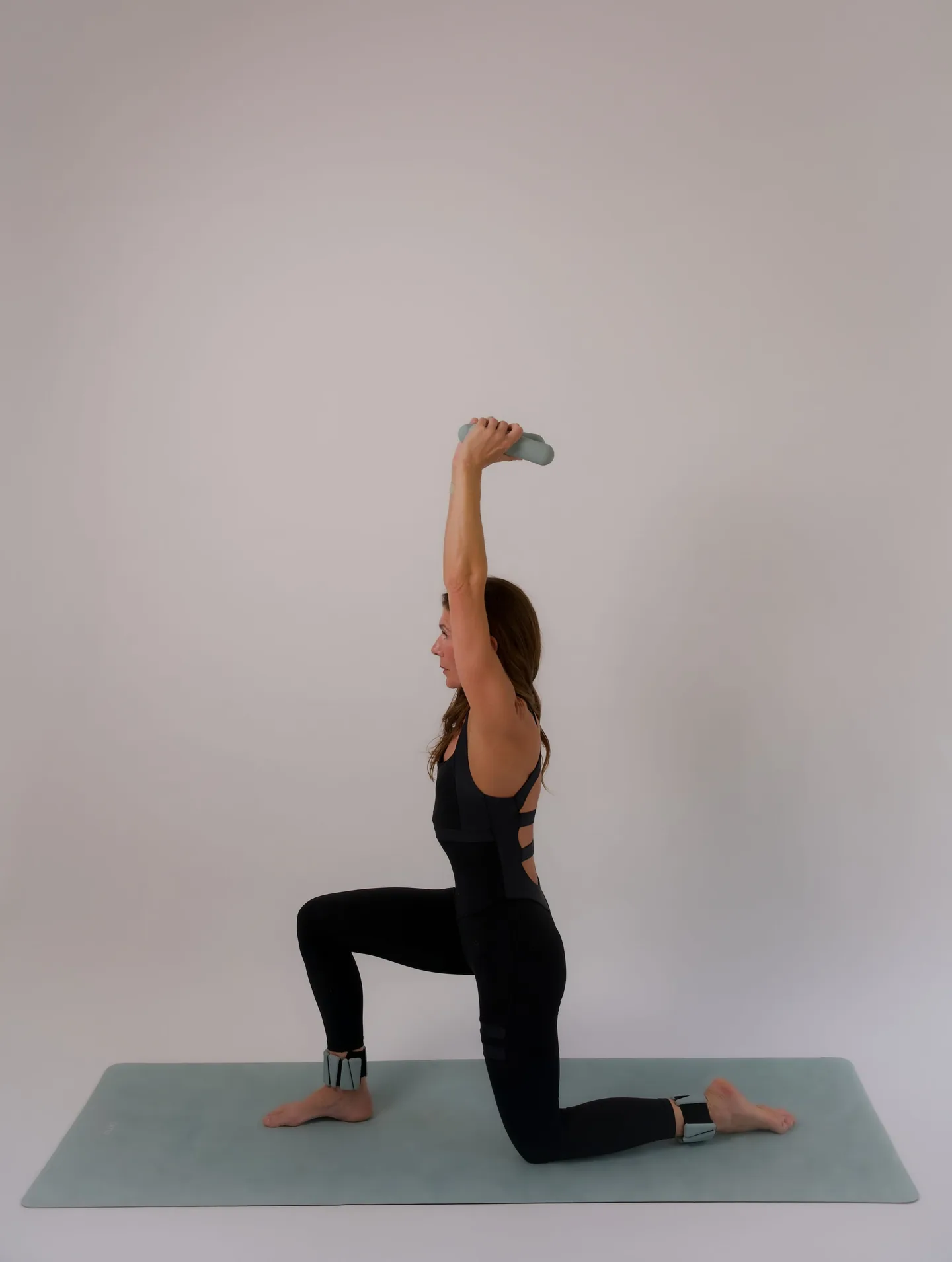 Yoga instructor kneeling in a lunge and lifting a dumbbell overhead in the studio