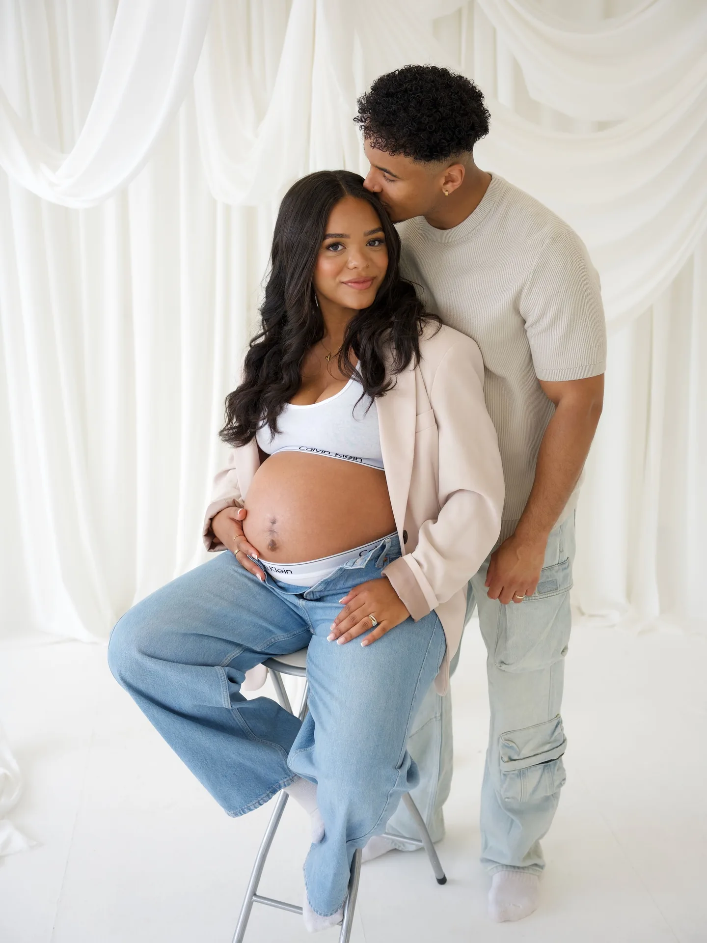 Expectant couple posing together in a bright cream studio