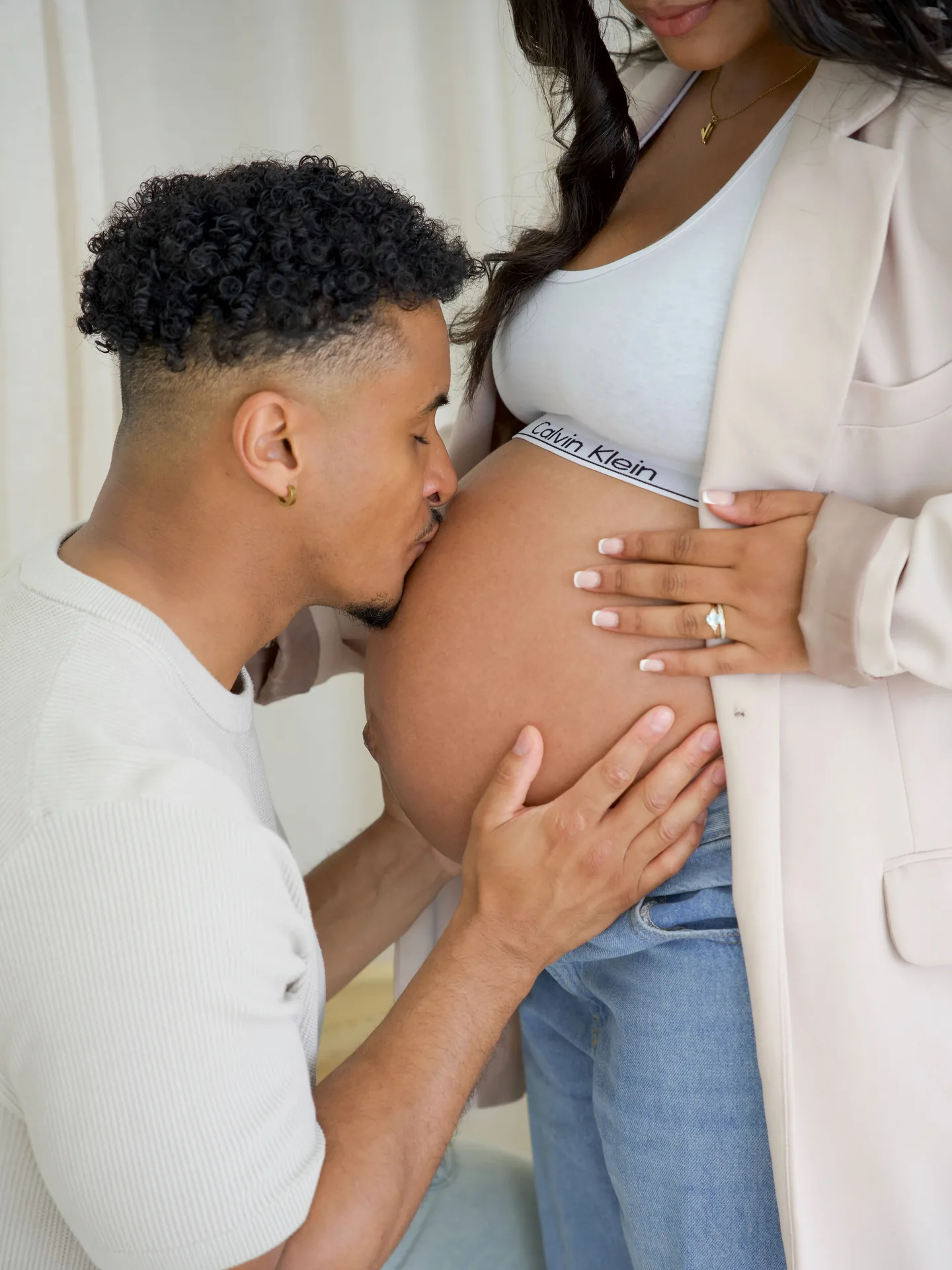 Partner kissing an expectant mother's bump during a bright studio maternity session