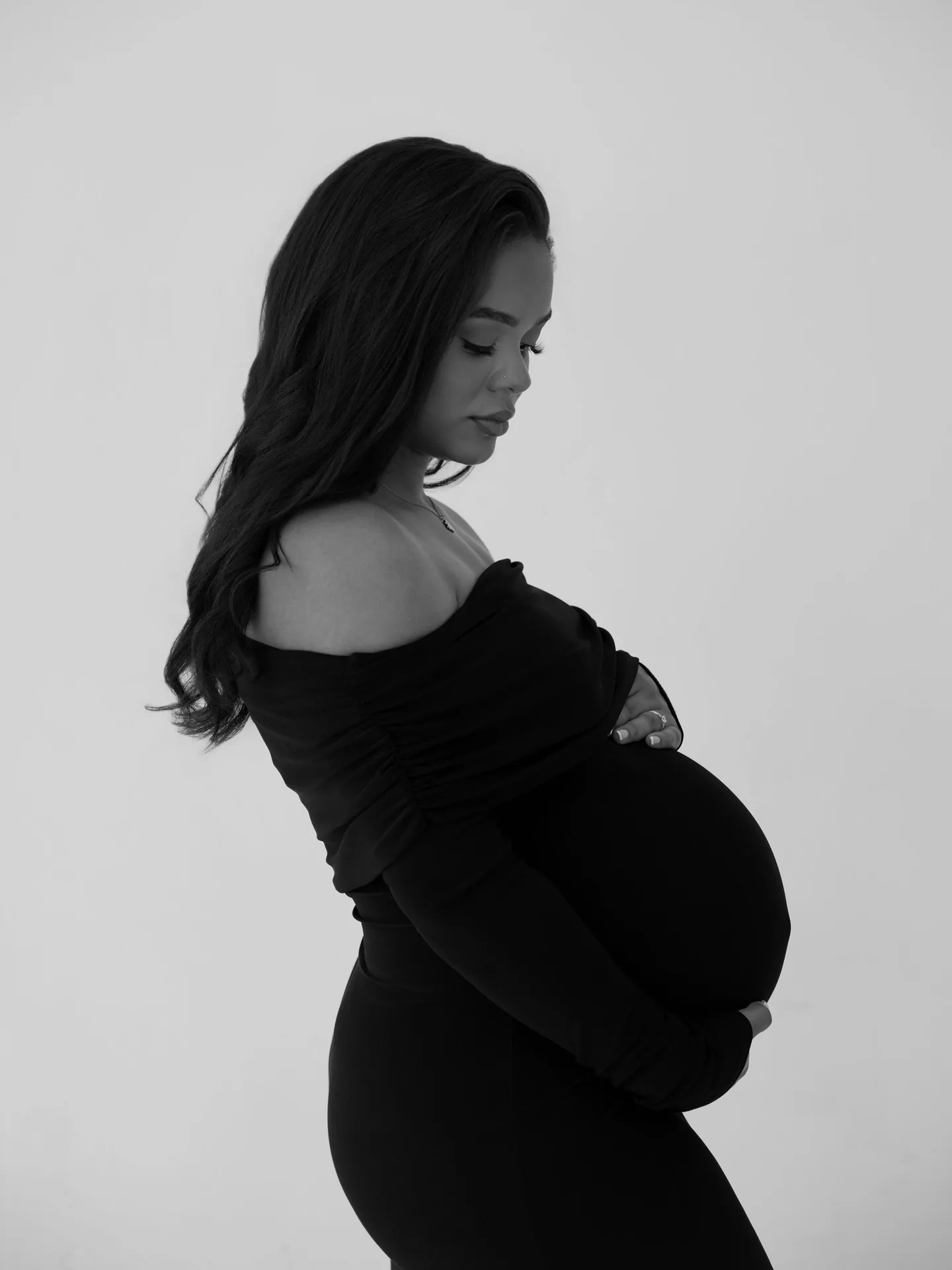 Black and white side-profile portrait of an expectant mother in a dark studio gown